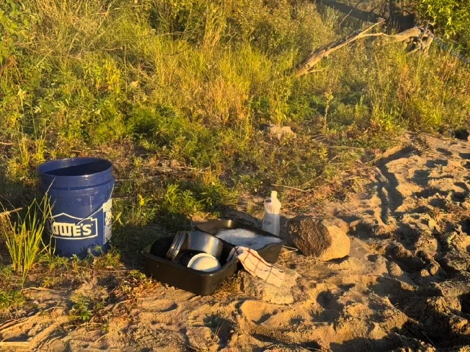 A wash tub of dishes and a bucket on the sand in low evening light