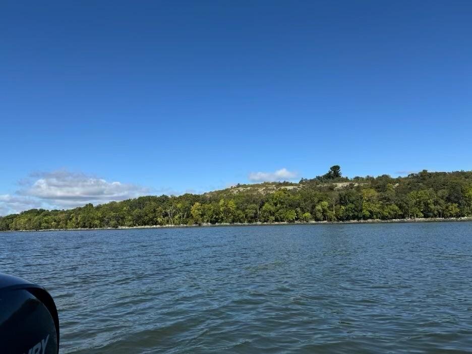 The tree-lined shoreline of Massacre Island seen from the boat, with the outboard cowling in the corner