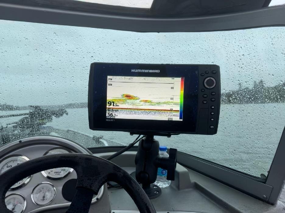 A Humminbird sonar screen showing fish marks stacked over 91 feet of water, seen through a rain-covered windshield